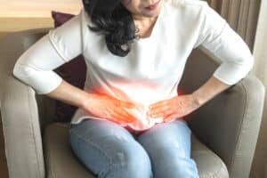 Woman sitting on couch, holding her lower abdomen as she experiences pelvic pain.