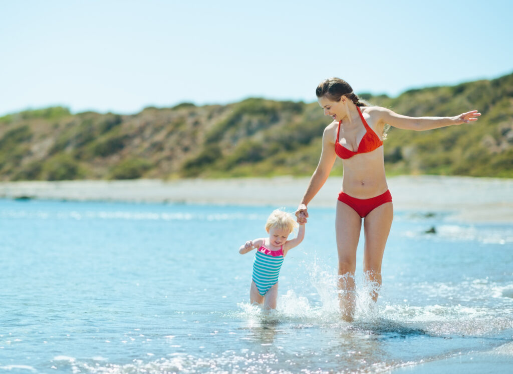 Mother plays with her young child in the water on the beach.